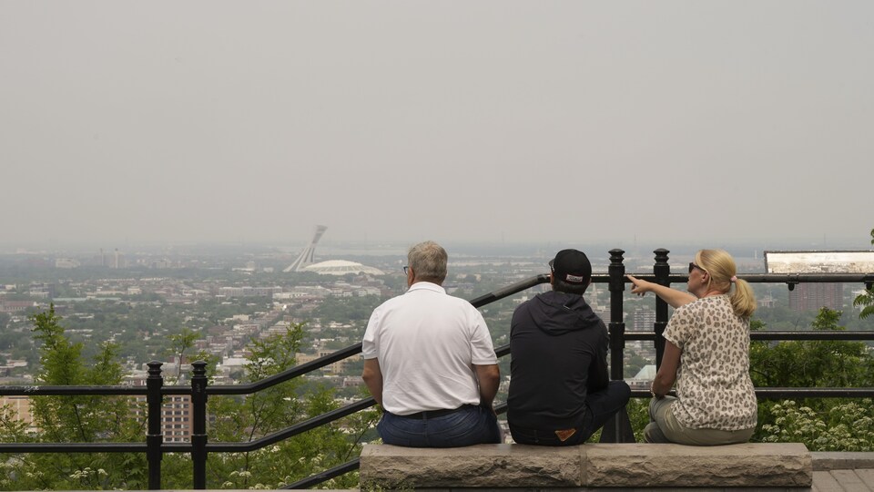 Des touristes regardent vers l'est depuis un belvédère sur le mont Royal, le lundi 5 juin 2023. Le ciel de la métropole est dense, envahi par le smog.