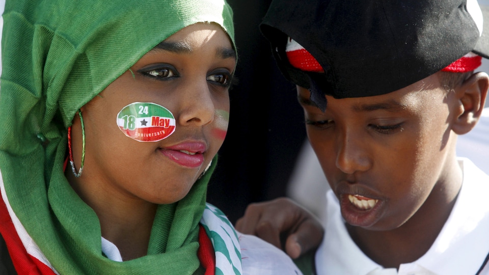 Une jeune fille avec un foulard vert qui recouvre ses cheveux et un autocollant sur la joue aux couleurs du Somaliland. Un jeune garçon est tout près d'elle.