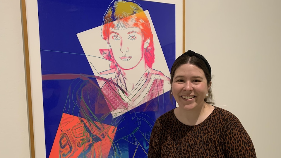 Sophie Hinch, souriante, est debout devant un portrait de l'ancien joueur de hockey professionnel Wayne Gretzsky créé par Andy Warhol.