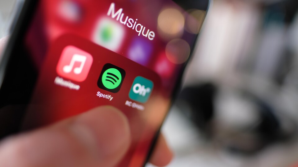 Le logo de l'application Spotify sur un téléphone et un doigt qui s'apprête à l'ouvrir.