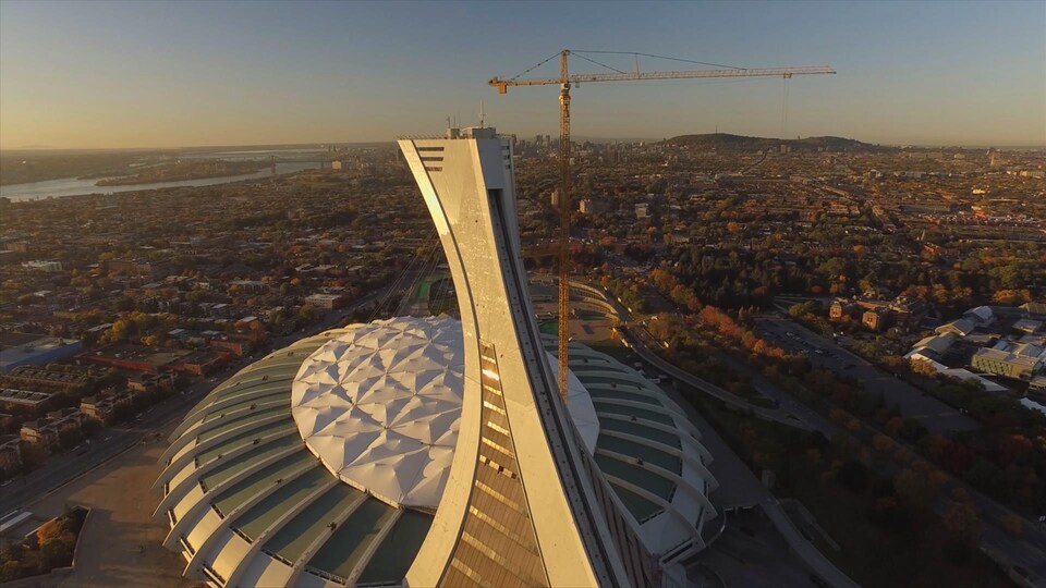 Le stade olympique vu de haut, illuminé par le soleil levant, avec la ville de Montréal en arrière-plan.
