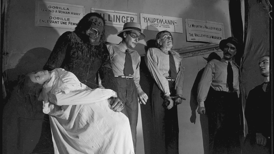 Photo en noir et blanc montrant les statues de cire d'un gorille tenant une femme évanouie et de trois hommes.