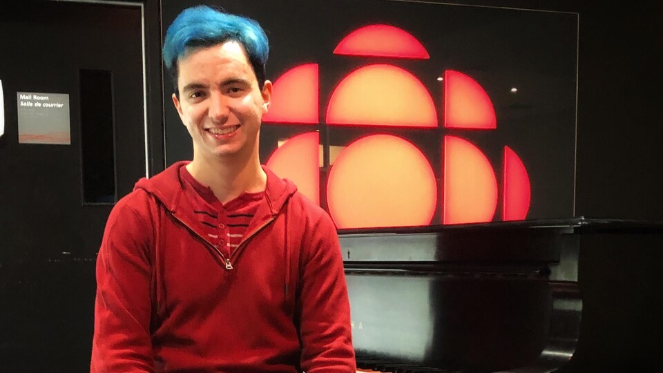 Stéphane Tétreault assis à côté d'un piano devant le logo de Radio-Canada.