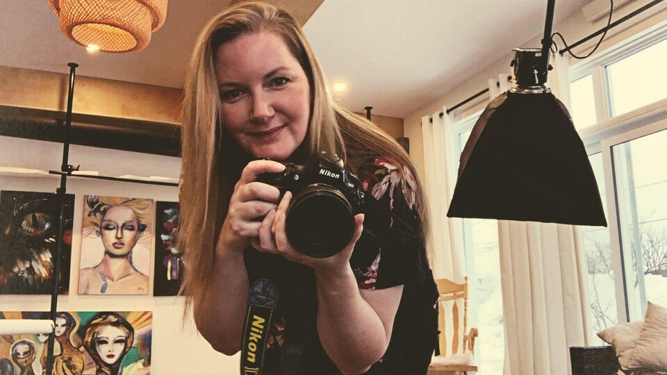 Une photographe dans son studio, caméra à la main.