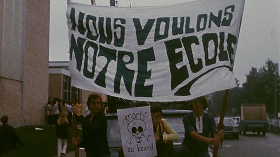 Des adolescents tiennent une grande bannière sur laquelle on peut lire « Nous voulons notre école ». 