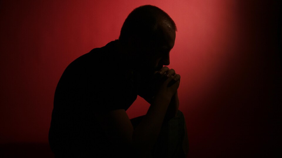 Un homme pensif devant un fond rouge et noir.