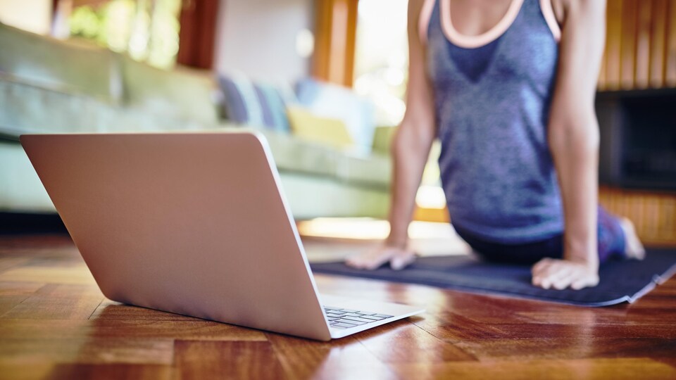 Une femme fait du yoga à la maison devant un ordinateur.
