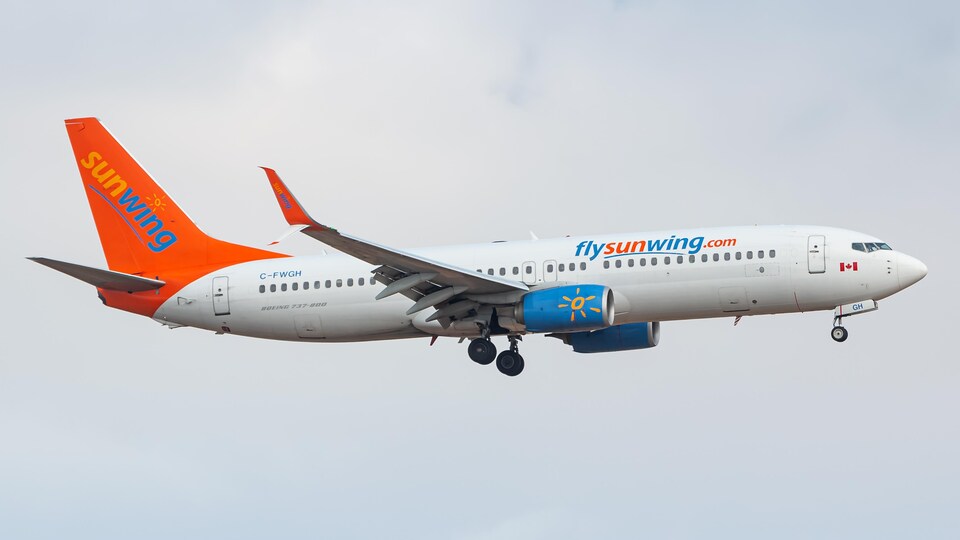 Un boeing 737 de la compagnie Sunwing Airlines en plein vol sur un fond de ciel nuageux.