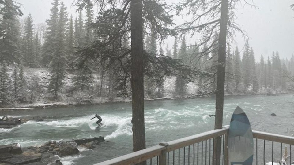 Un homme en combinaison fait du surf sur une rivière, l'hiver. 