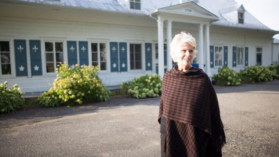 Sylvie Lauzon est souriante devant le presbytère par une journée ensoleillée.