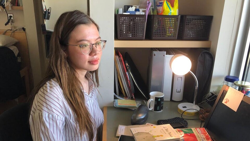 Une jeune fille est assie devant son ordinateur dans une petite chambre.