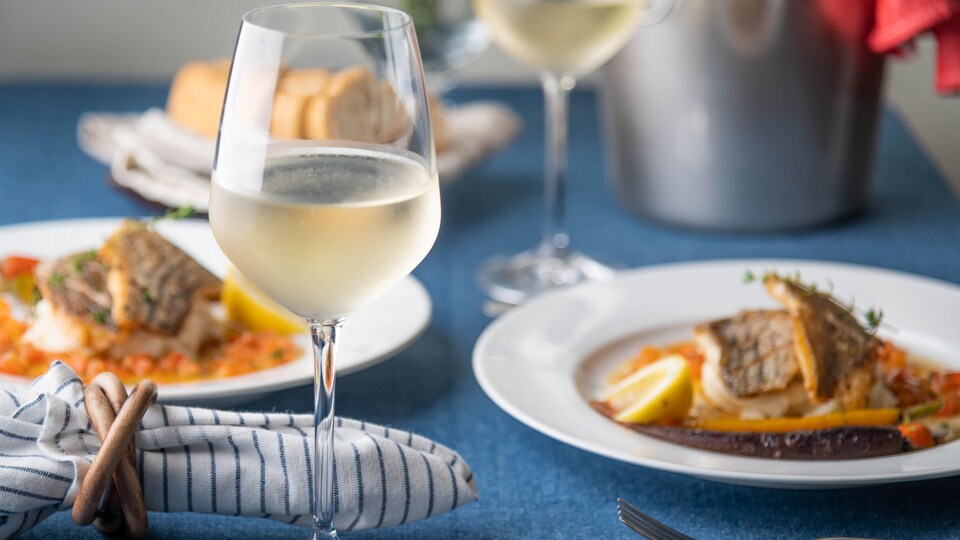 Table dressée avec deux plats de poisson poêlés et du vin blanc.
