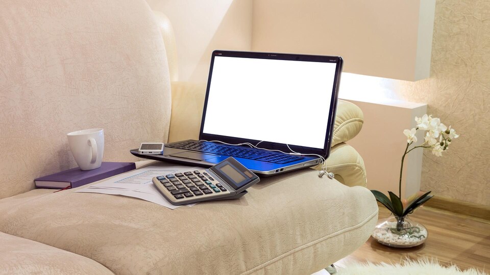 Un ordinateur de travail, une calculatrice, une tasse et un téléphone cellulaire posés sur un sofa. 