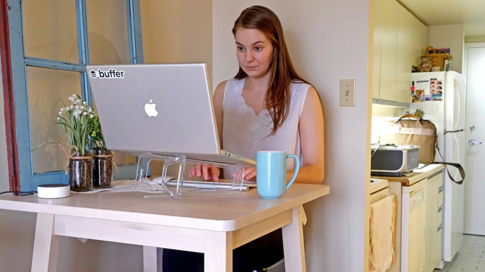 Une femme travaille avec un ordinateur portable sur une petite table devant sa cuisine.