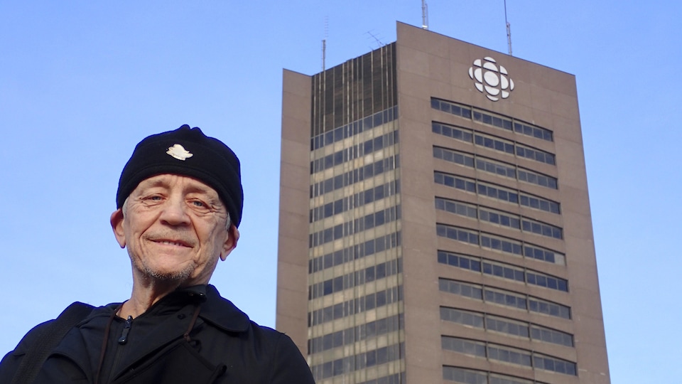 Vue en contre-plongée d'un homme devant une tour brune arborant le logo de Radio-Canada.
