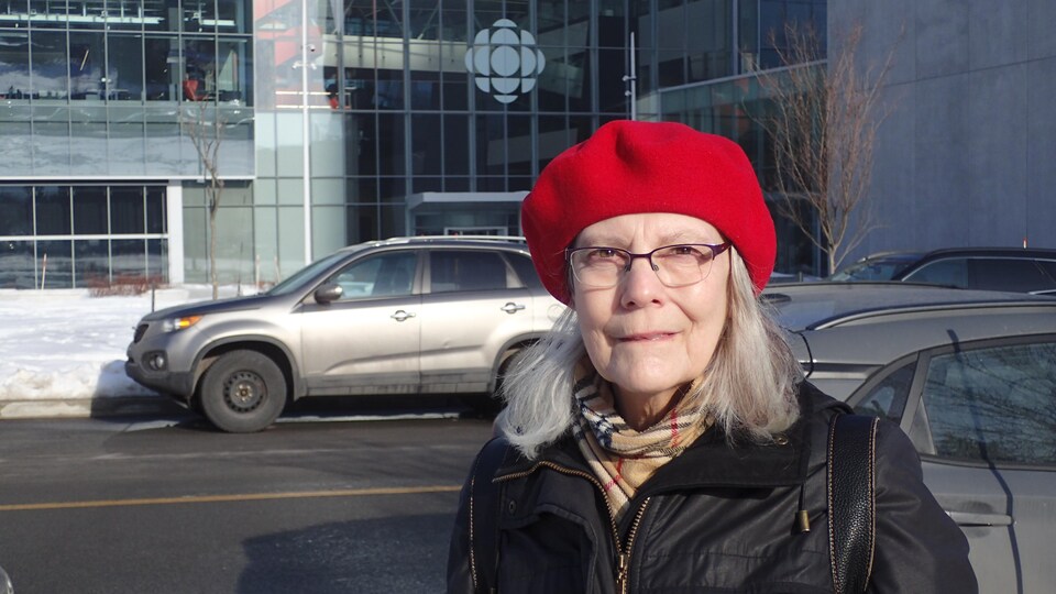 Une femme devant un édifice vitré arborant le logo de Radio-Canada.       