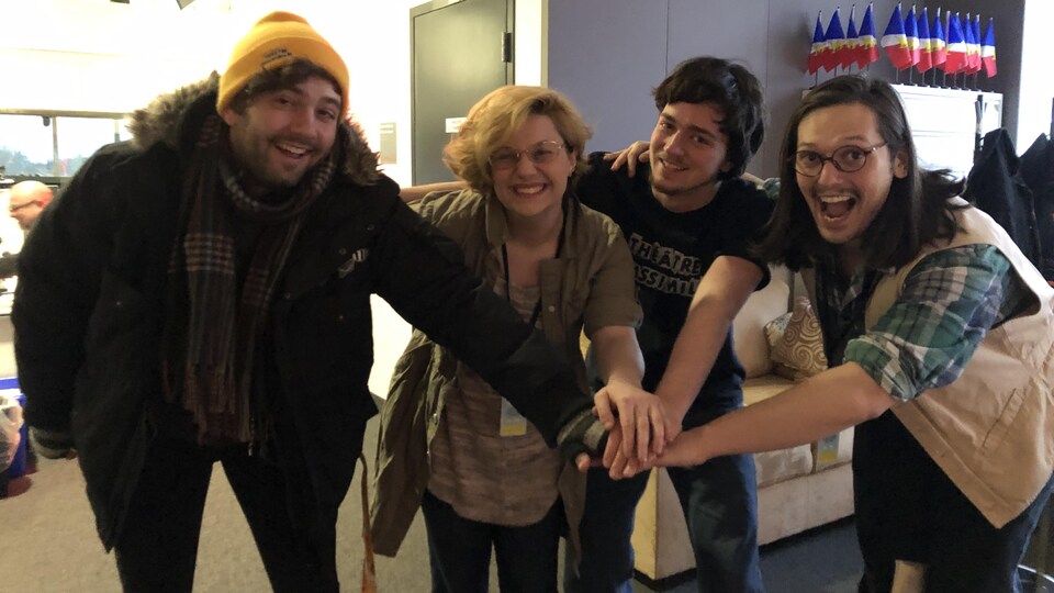 Zac Comeau, Lily Swim, Olivier Blais et Thibault Jacquot-Paratte regardent l'objectif avec leur main au milieu, une sur l'autre, dans le studio de Radio-Canada Halifax.