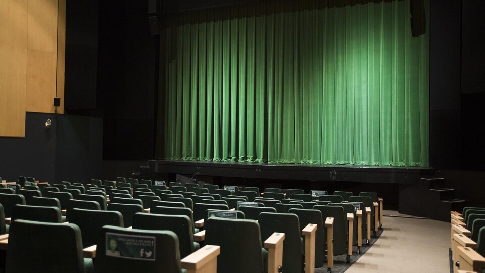 Une salle de théâtre dont le rideau est vert et dont les sièges sont verts. 