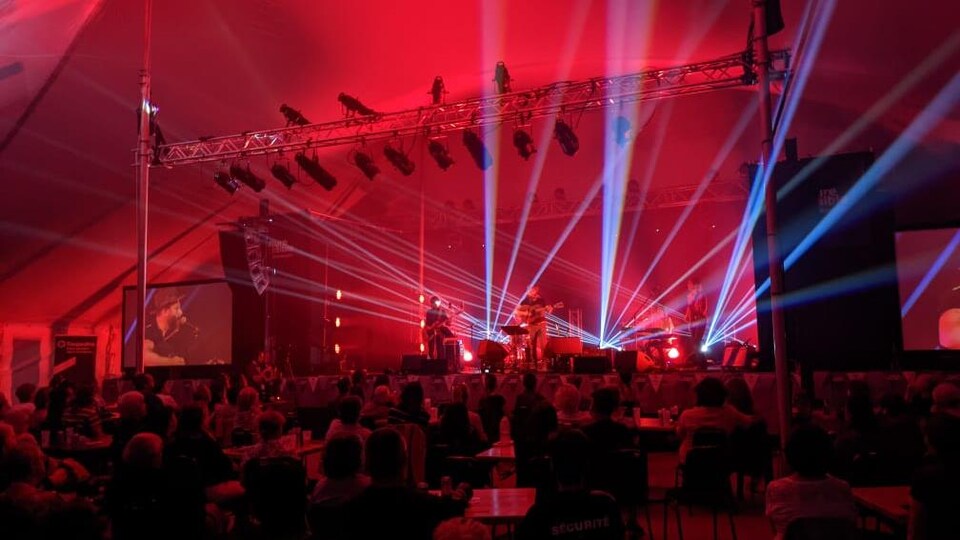 Des gens sur une scène éclairée par des faisceaux lumineux et le public dans la salle.