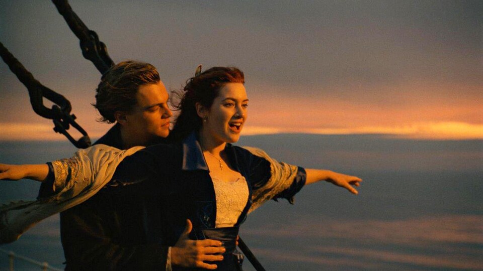 Un homme et une femme sont sur un navire. La femme étend les bras sur les côtés, l'homme la tient par la taille.