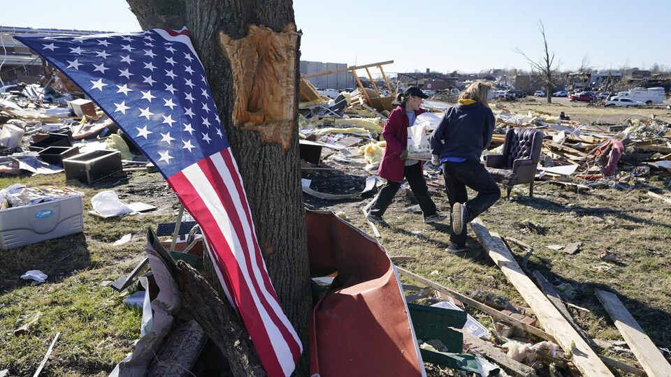 Un drapeau est suspendu à un arbre. De nombreux débris jonchent le sol, dont des meubles et des matériaux servant à la construction d'habitation.  
