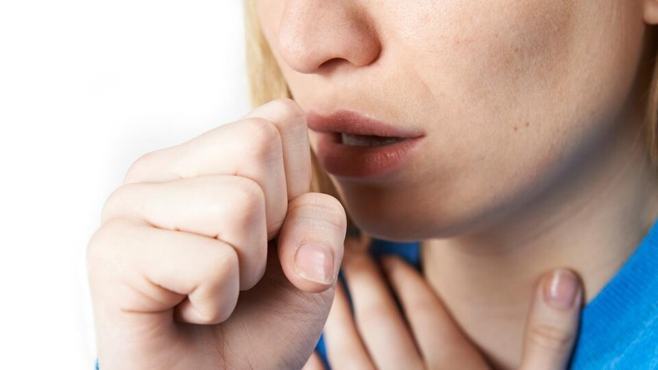Visage d'une femme qui tousse. Elle a une main sur la gorge et une autre devant sa bouche.