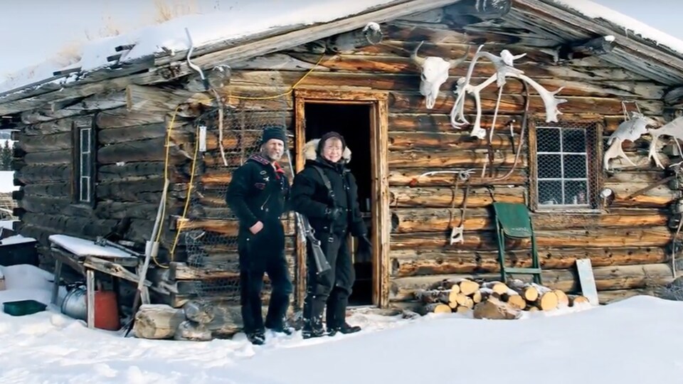 Un homme et une femme posent devant une cabane en bois en hiver.