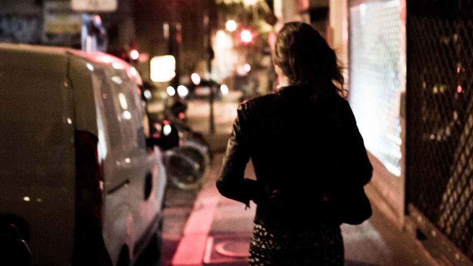 Une femme marche dans la rue, la nuit. 