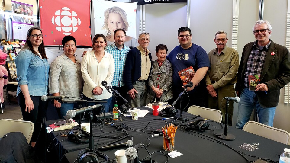 Quatre femmes et quatre hommes avec l'animateur de radio Éric Robitaille dans un Salon du livre à Hearst.