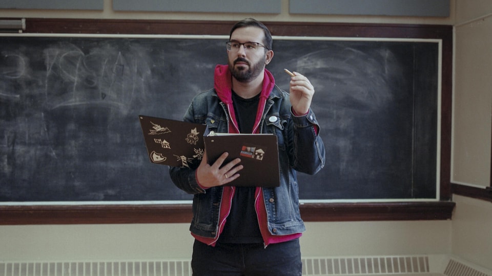 Trevor Murphy se tient debout, cartable d'école et crayon à la main, devant un tableau dans une salle de classe.
