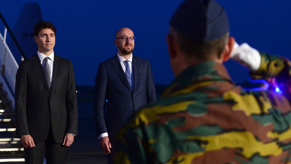 Le premier ministre Justin Trudeau se tient à côté de son homologue belge, Charles Michel, à sa descente d'avion. Devant eux, un soldat belge fait le salut militaire.