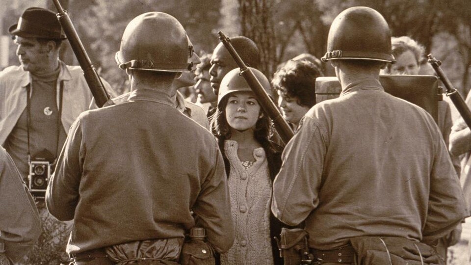 Une jeune manifestante portant un casque fait face à des policiers casqués et armés lors d'une manifestation contre la guerre du Vietnam devant la Convention nationale démocrate à Chicago en Illinois, août 1968.