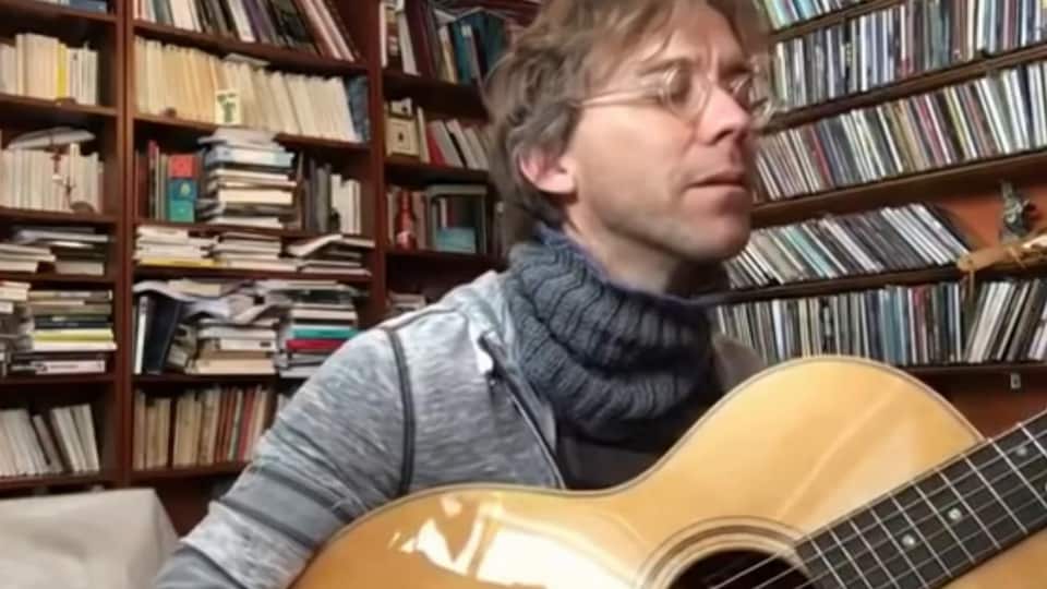Fred Pellerin joue de la guitare dans sa bibliothèque.