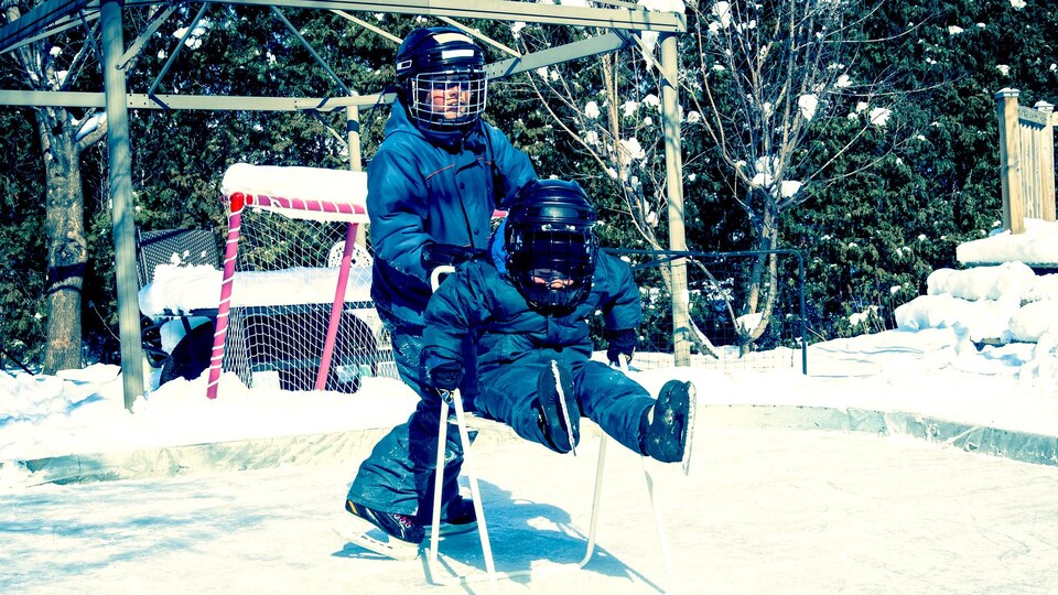 Un grand frère aide son jeune frère sur une patinoire extérieure.
