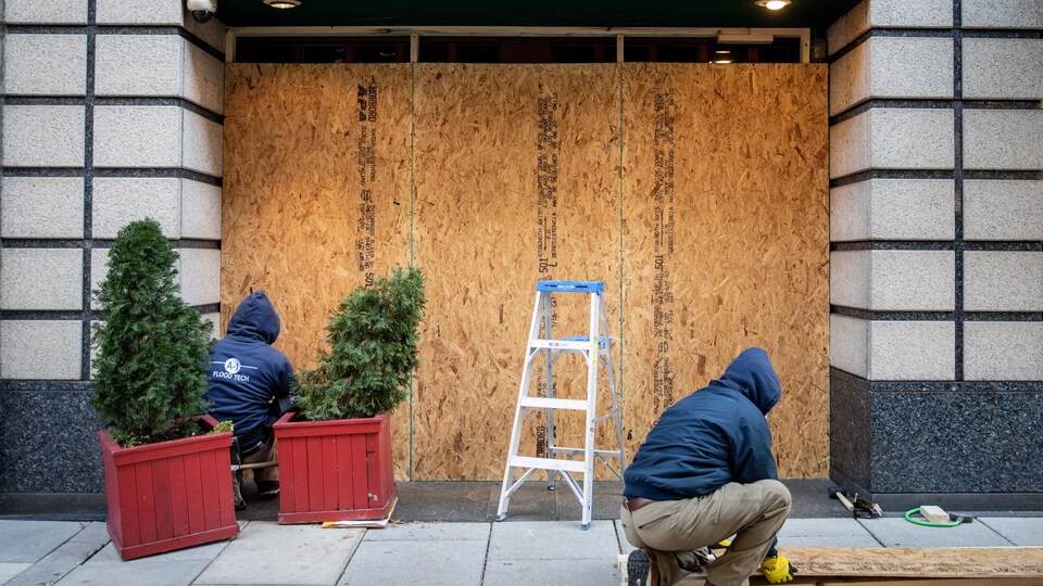 Deux hommes travaillent à barricader les vitrines devant un magasin à Washington.