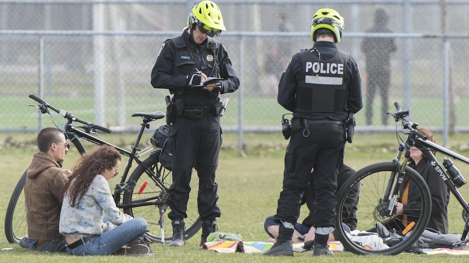 Deux policiers écrivent des contraventions alors que des gens sont assis par terre.