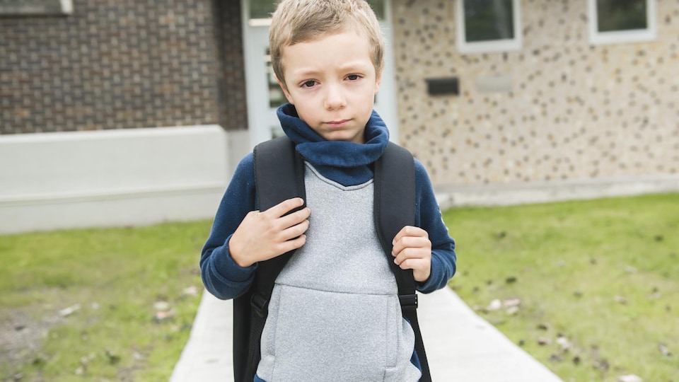Un jeune garçon part pour l'école en tenant son sac à dos. 