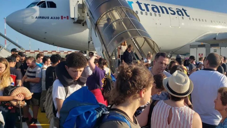 Photo de passagers sur le tarmac près d'un avion et d'autres qui descendent de l'appareil par un escalier.