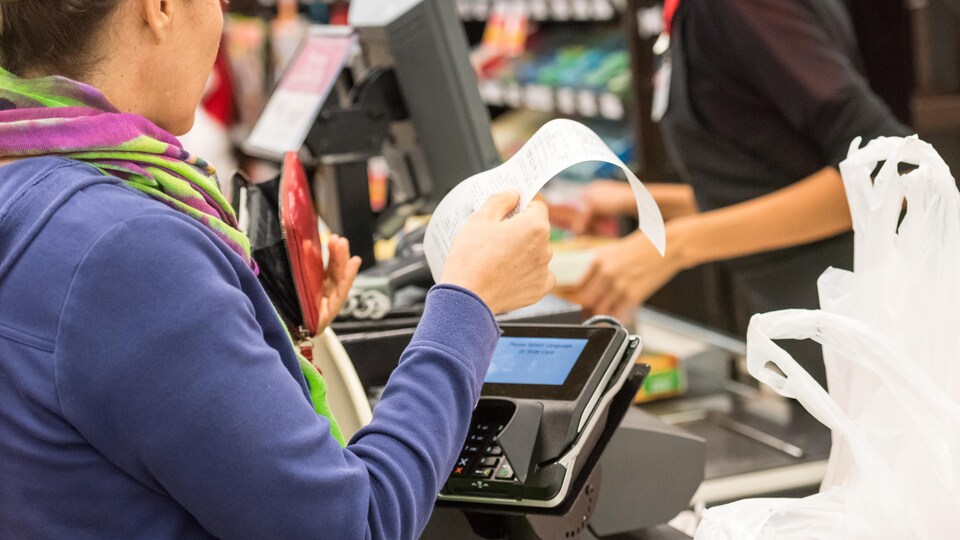 Une cliente inspecte sa facture à la caisse d'un grand magasin.