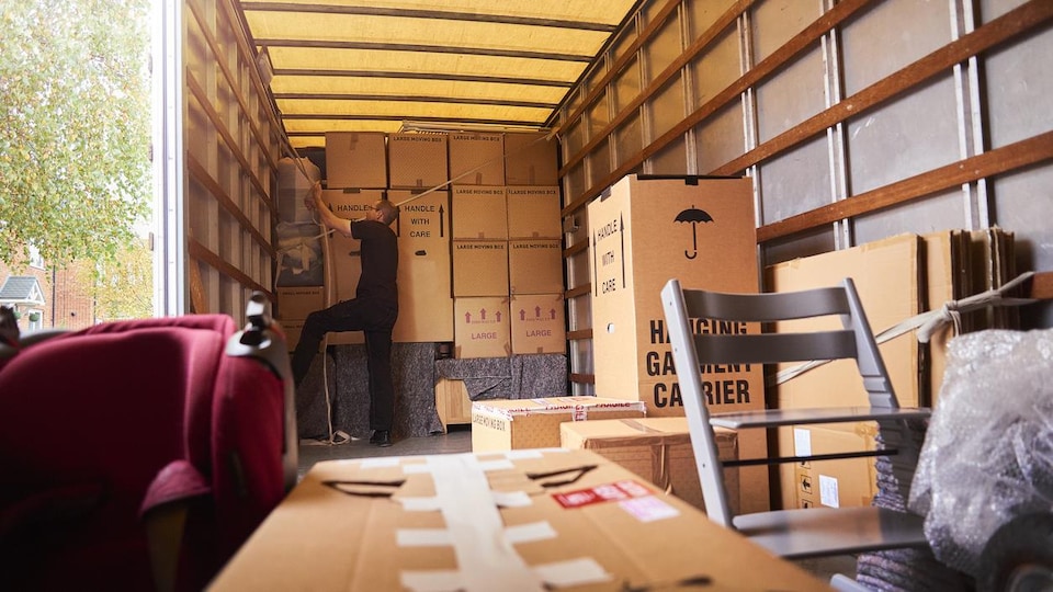 Un homme organise l'intérieur d'un camion rempli de boîtes et de meubles.