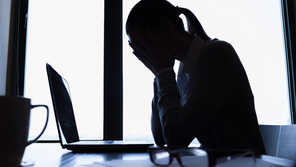 Une femme se tient la tête, assise à son bureau devant un ordinateur.