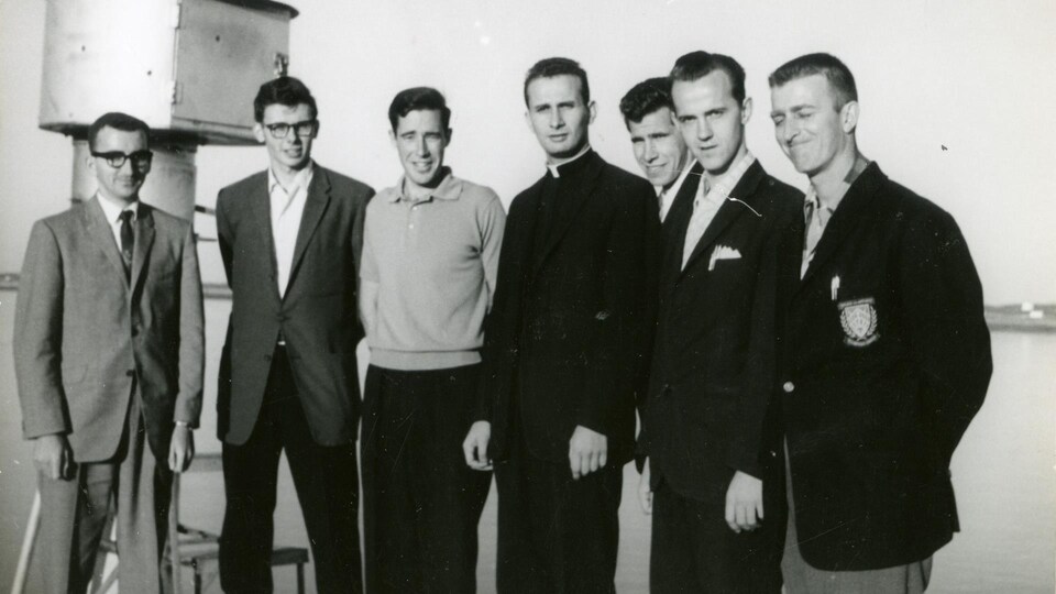Une photo en noir et blanc de sept hommes, dont un prêtre.