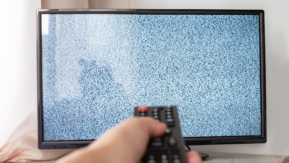 Une main tient une télécommande devant une télé qui n'affiche pas d'image. 