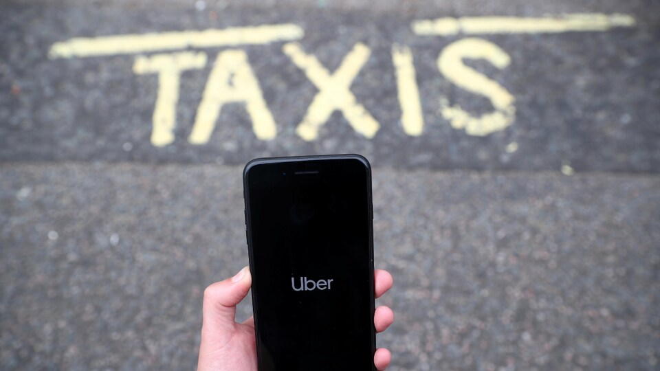 Un téléphone intelligent affichant l'application Uber, au-dessus d'une chaussée sur laquelle il est écrit : « TAXIS ».