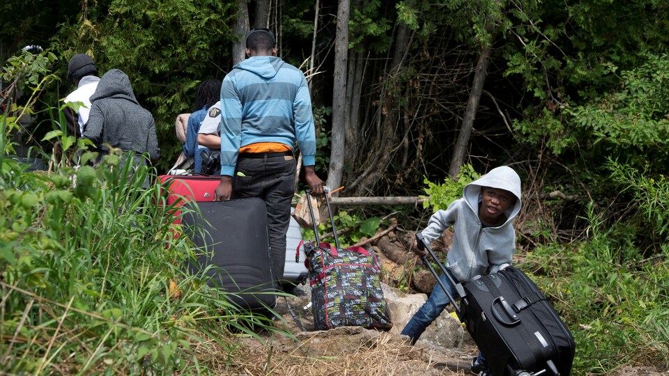 Une famille transporte des bagages alors qu'ils traversent la frontière pour demander asile au Canada.
