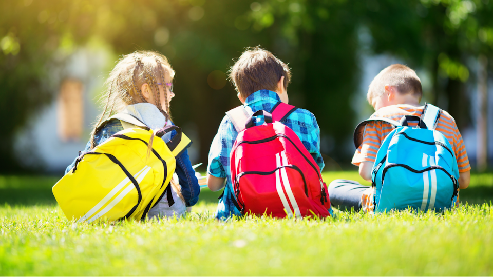 Une fille et deux garçons sont assis dans un parc avec leurs sac à dos.