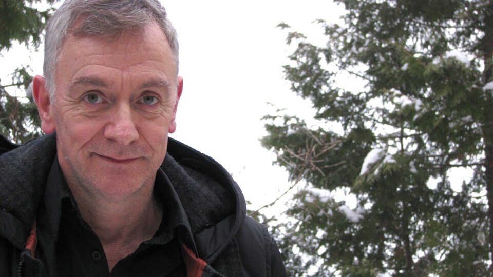 Le dramaturge et scénariste Michel Marc Bouchard, dehors l'hiver, devant des conifères enneigés.