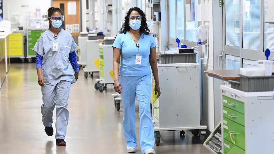 Deux infirmières avec masque et lunettes de protection marchent dans un couloir d'hôpital.