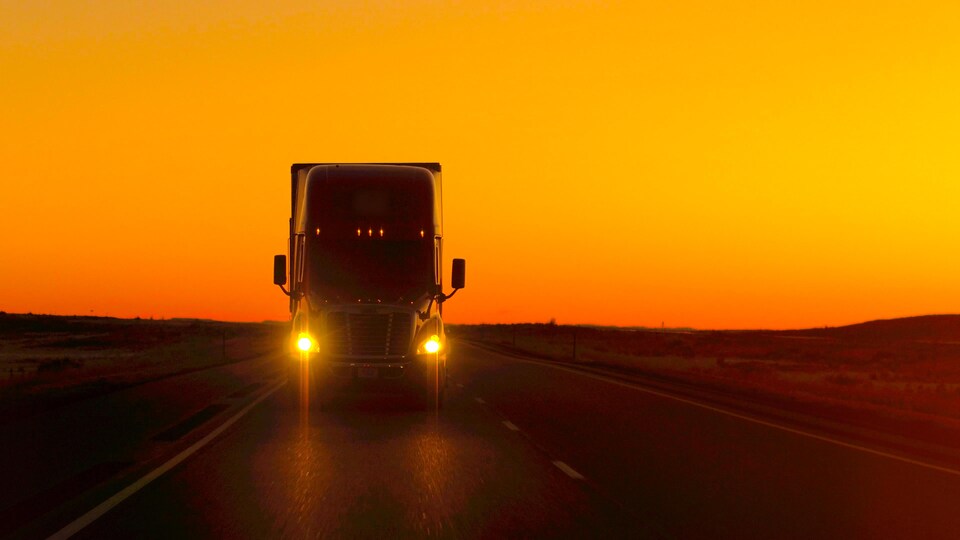 Un camion roule sur une route au moment où le soleil se couche.