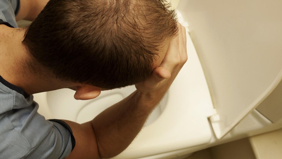 Un homme est accoudé sur la cuvette de sa toilette.